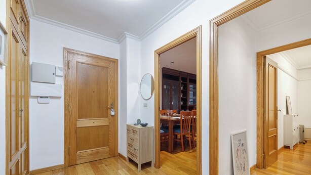 A hallway with wooden doors, a dining area with a table and chairs, and a blue rug on the floor. - Encantador Piso con Parking (Vigo)
