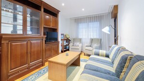 A living room with a wooden cabinet, a television, two armchairs, a sofa, and a lamp. - Encantador Piso con Parking (Vigo)