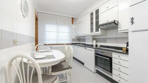 A modern kitchen with white cabinets, a round dining table, and a built-in oven. - Encantador Piso con Parking (Vigo)