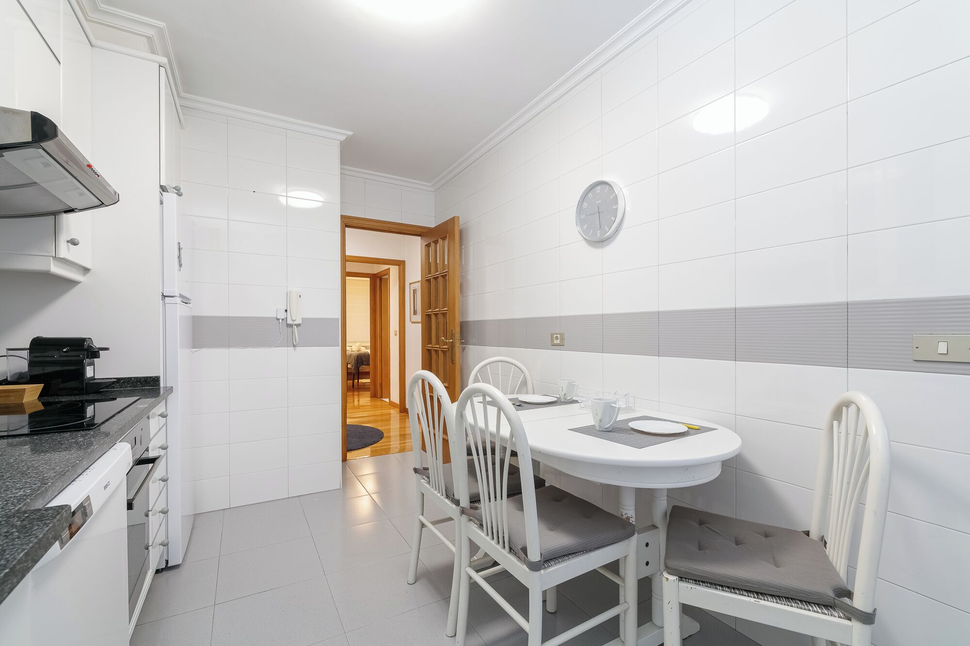 Una cocina moderna con gabinetes blancos, estufa integrada y un área de comedor con mesa y sillas blancas.
