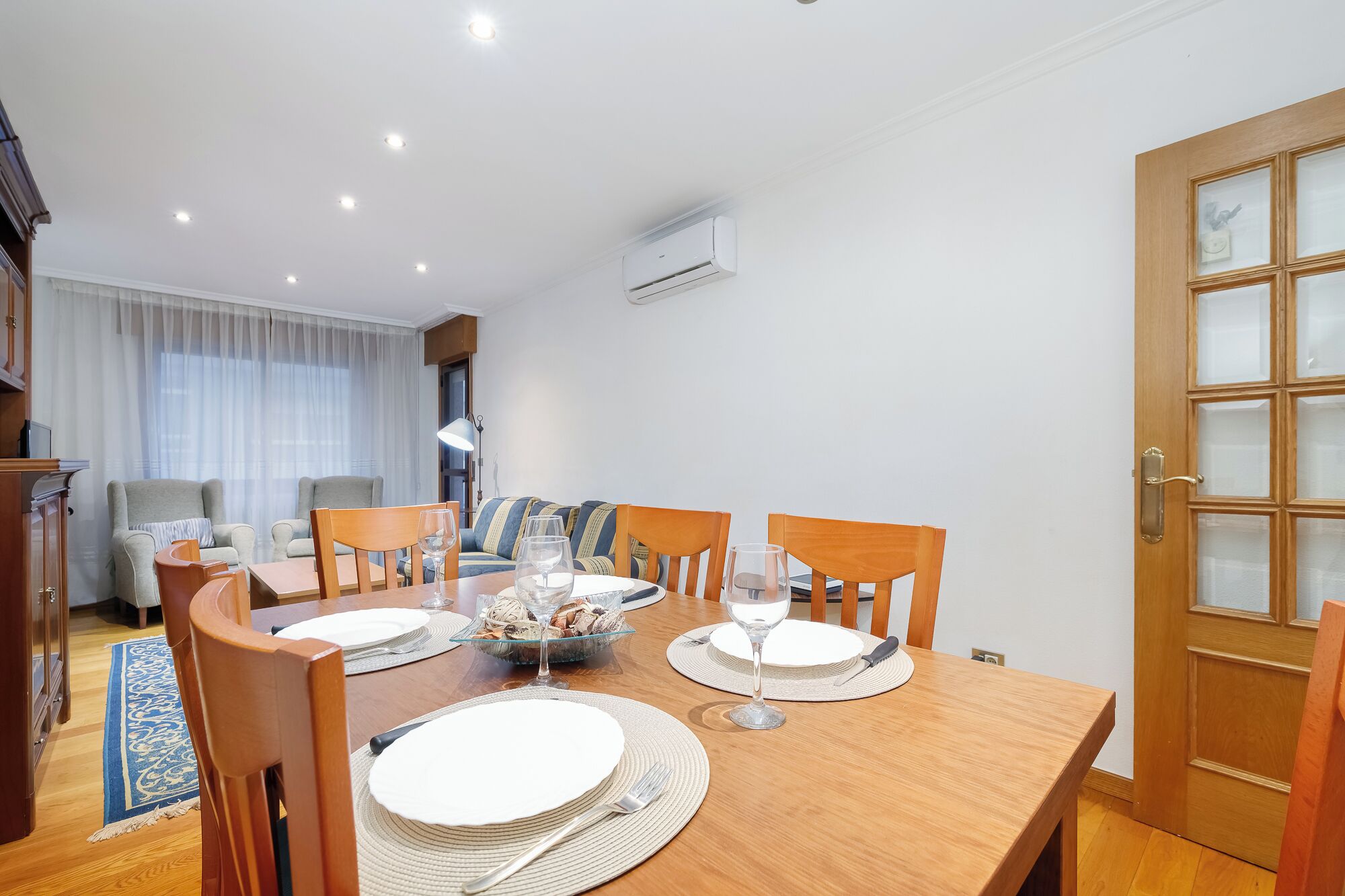 A dining area with a wooden table set for four, chairs, and a buffet with bread.