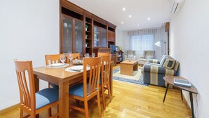 A dining area with wooden chairs and a table set for four, a living room with a sofa and armchairs, and a built-in wooden cabinet with glass doors. - Encantador Piso con Parking (Vigo)