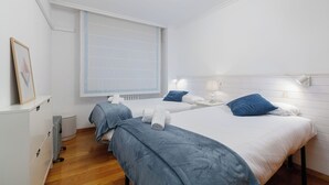A hotel room with two beds, a radiator, a window with blinds, and a bedside table with a lamp. - Encantador Piso con Parking (Vigo)