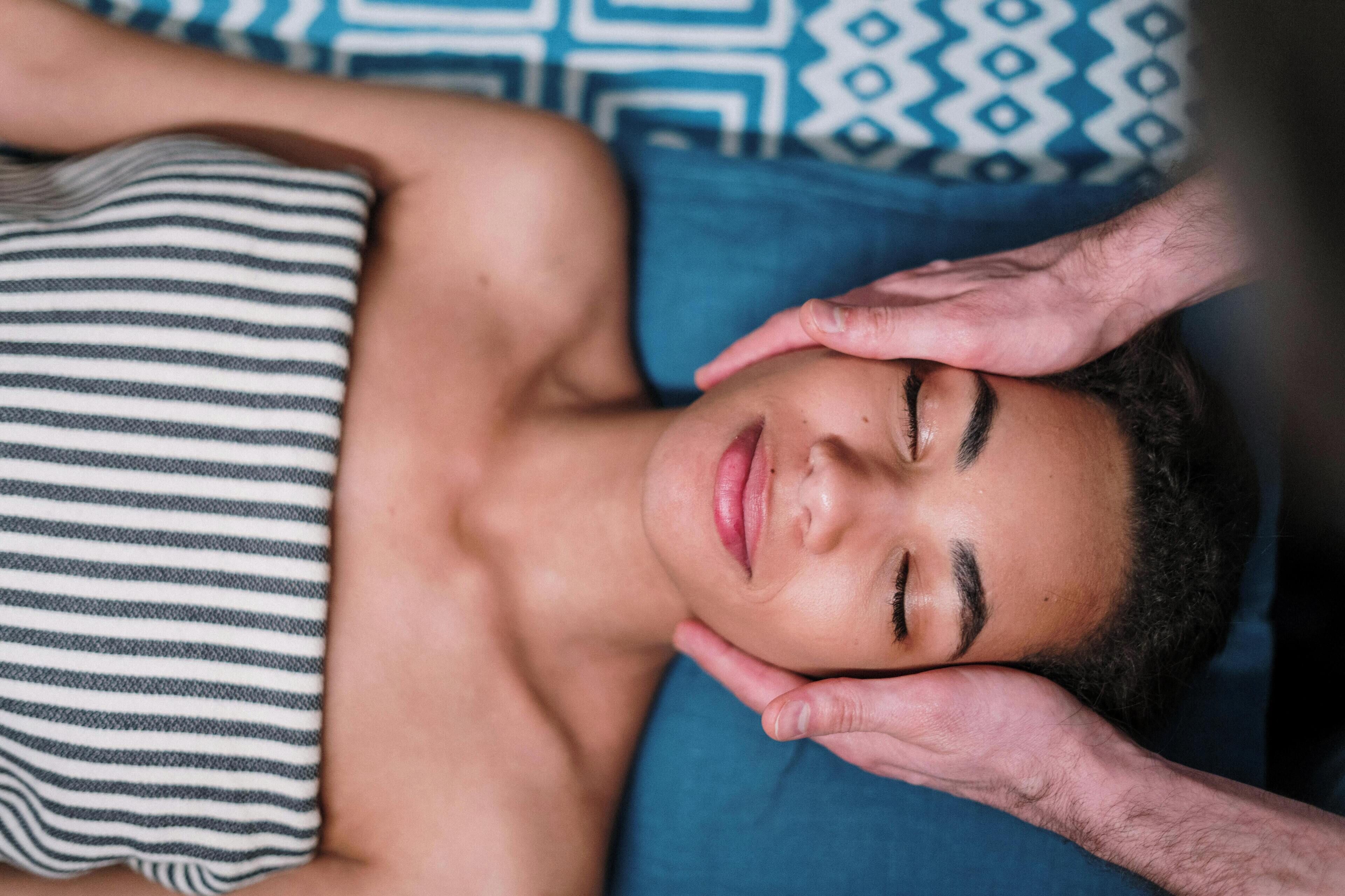 Une personne allongée sur un lit, avec un oreiller à rayures et un autre à motifs.