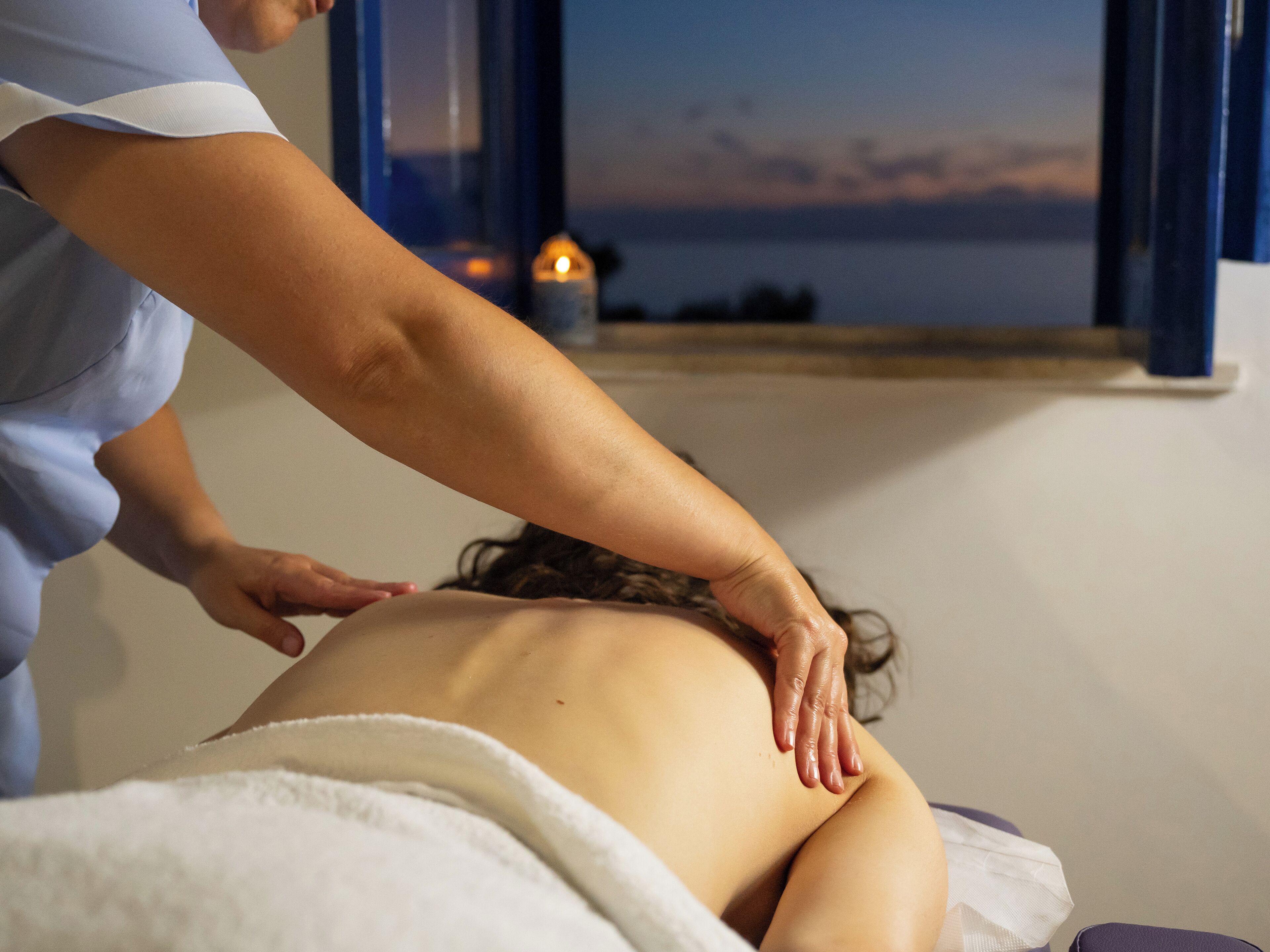 A massage therapy session in a room with a view of the sea at sunset.