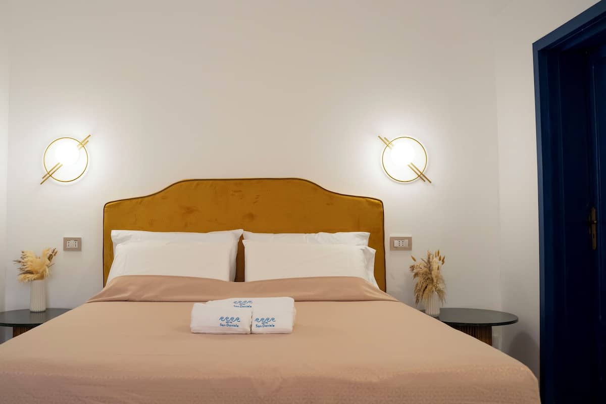 Een netjes opgemaakt bed met een hoofdeinde, twee nachtkastjes met lampen en een handdoek met een logo.