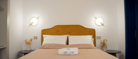 A neatly made bed with a headboard, two bedside tables with lamps, and a towel with a logo.