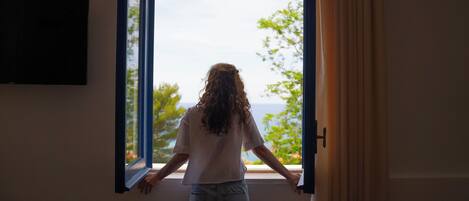 A person standing by an open window with a view of trees and a body of water.