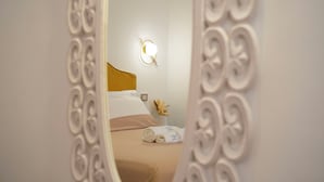 Een slaapkamer met een bed, nachtkastje, een wandlamp en een decoratieve spiegel.