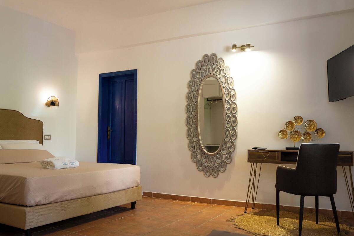 Een slaapkamer met een bed, een bureau, een stoel, een spiegel en een televisie.