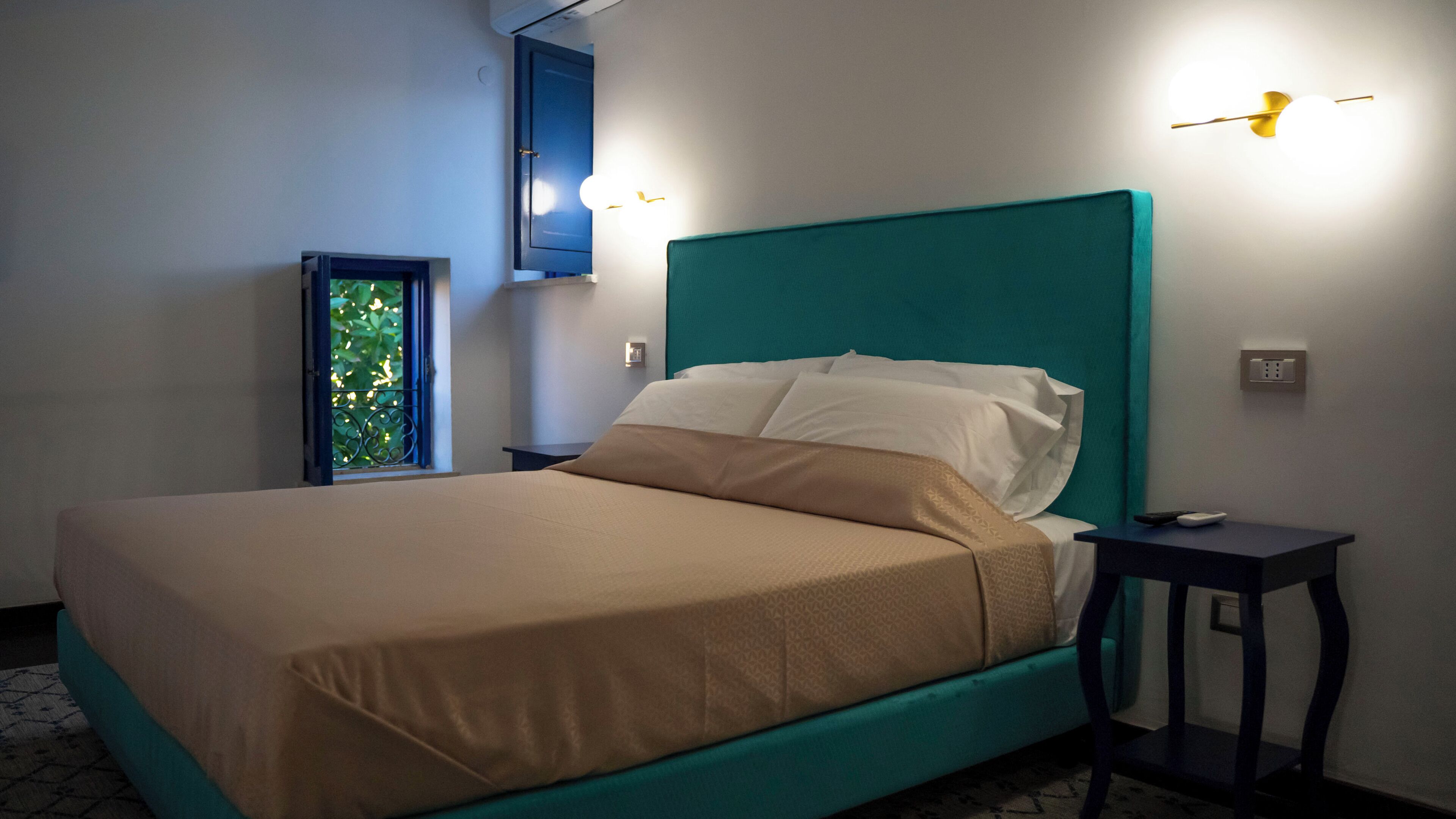 A neatly made bed with a teal headboard in a hotel room.
