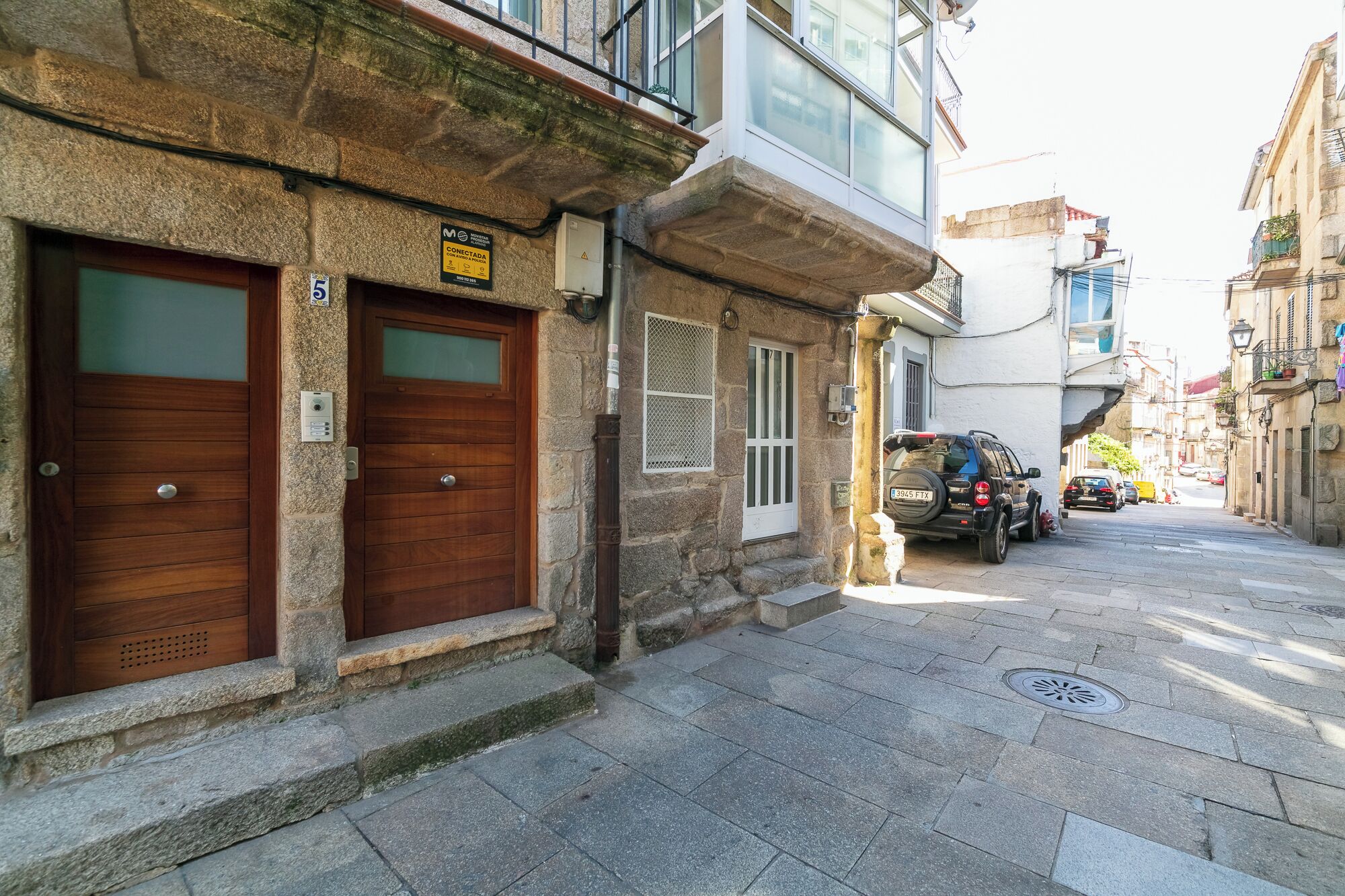 Une rue étroite bordée d’immeubles en pierre, avec deux portes en bois et un véhicule garé.