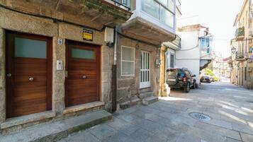 Une rue étroite bordée d’immeubles en pierre, avec deux portes en bois et un véhicule garé.