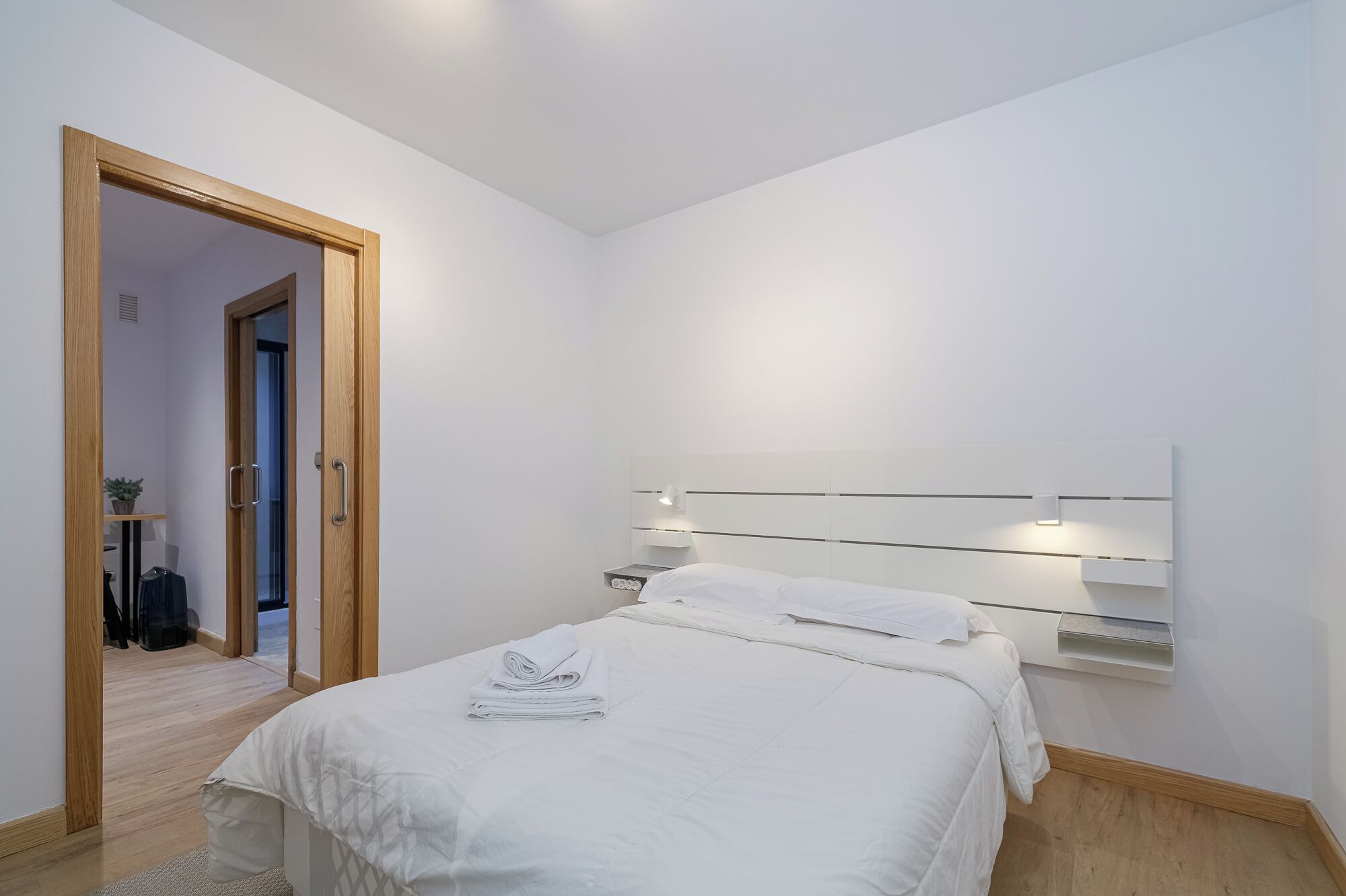 Una habitación de hotel moderna con una cama, mesita de noche y una lámpara de pared.
