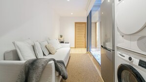 A modern bedroom with a sofa, a washing machine, and a wooden door. - Oasis de Elegancia (Vigo)