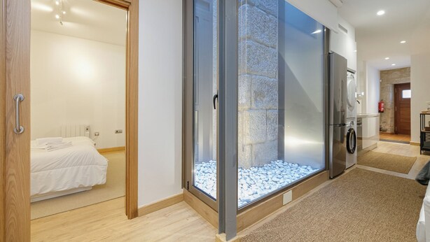 A modern hotel room with a sliding glass door leading to a balcony, a bed, a built-in washing machine, and a stone wall feature. - Oasis de Elegancia (Vigo)