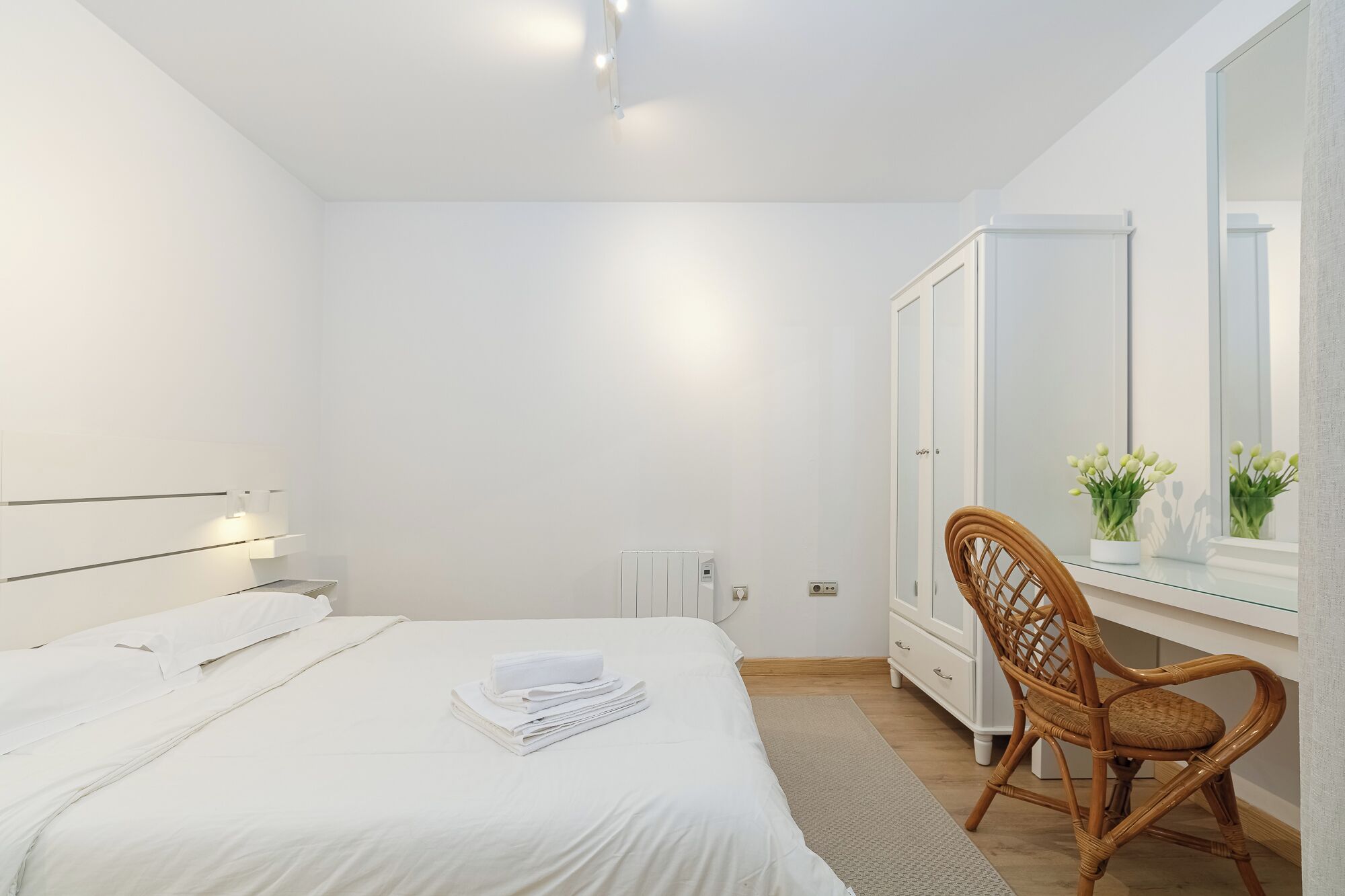 Un dormitorio minimalista con cama, mesita de noche, silla, armario y espejo.