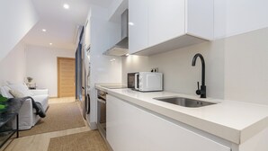 A modern kitchen with white cabinetry, a stainless steel sink, and a black faucet. - Oasis de Elegancia (Vigo)