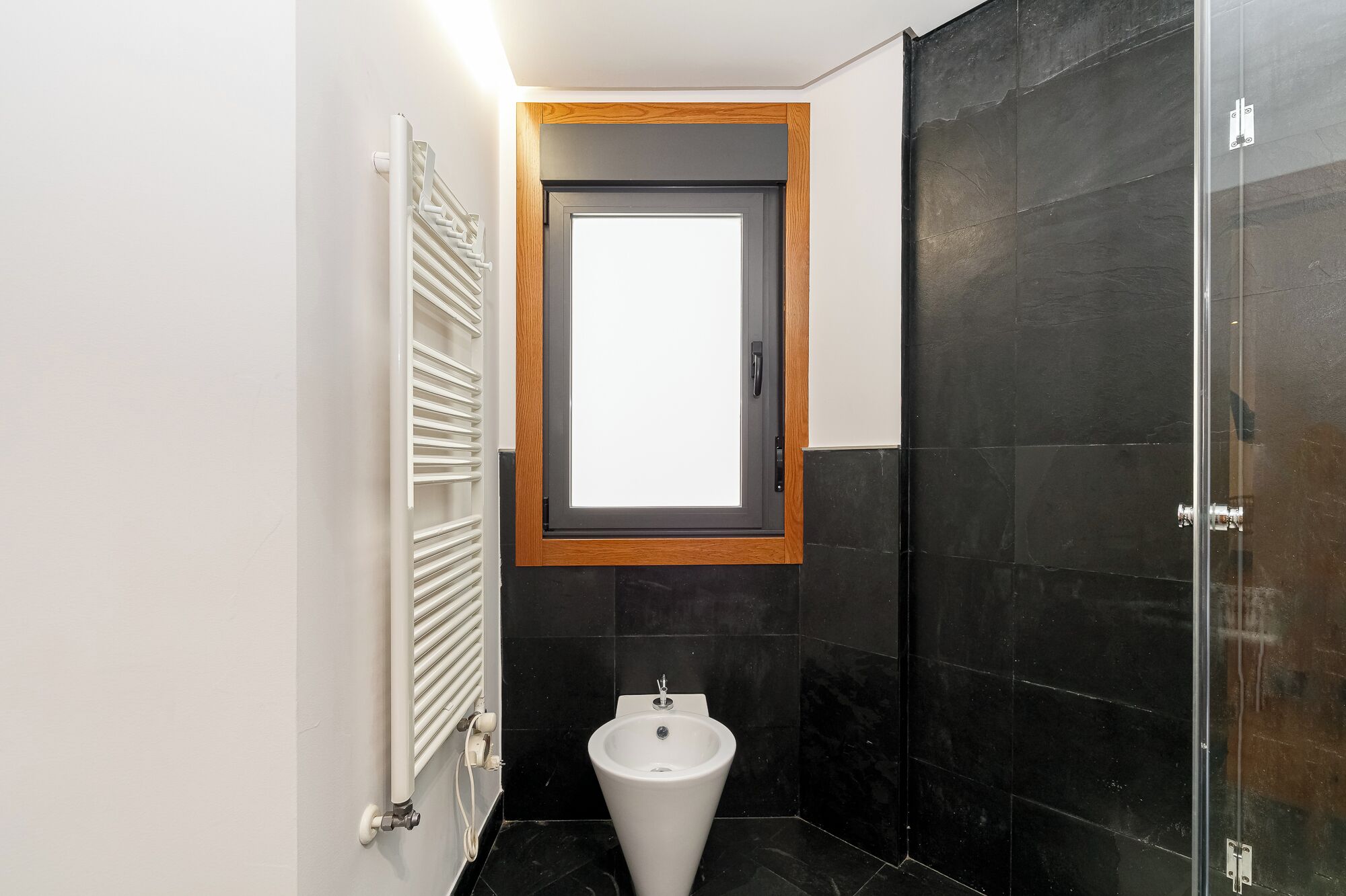 Une salle de bain avec un radiateur blanc, un lavabo sur colonne et un espace douche.