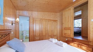 Ett rum med träpanel på väggarna, en säng, ett badrum som syns genom en glasdörr och ett stort fönster.