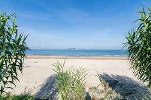 Ein Strand mit blauem Himmel, ruhigem Wasser und in der Ferne liegenden Inseln.