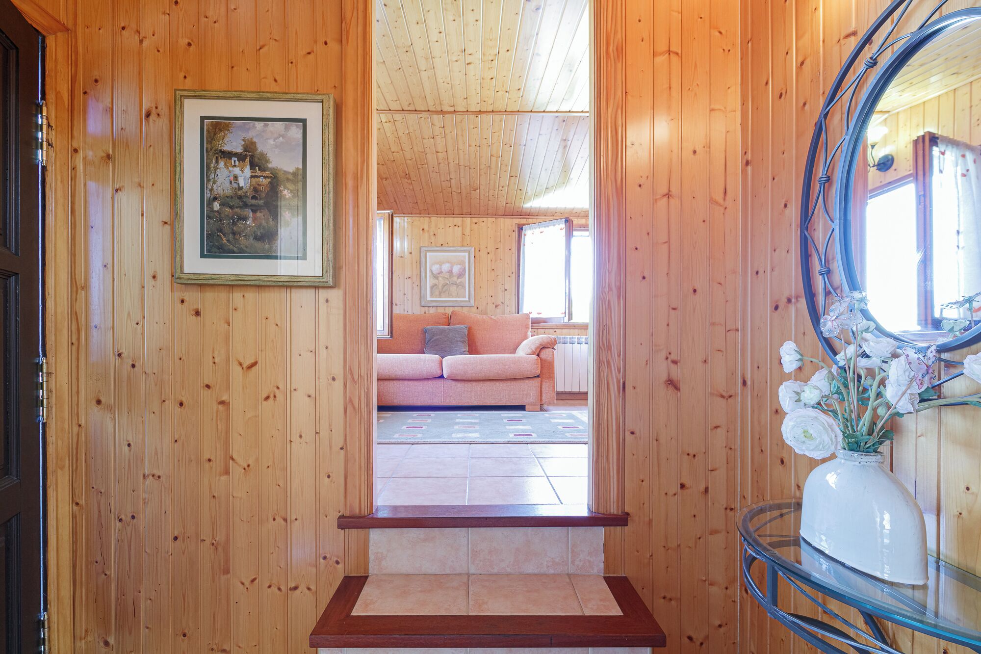 Un interior de madera con un sofá, un cuadro enmarcado y un florero con flores.