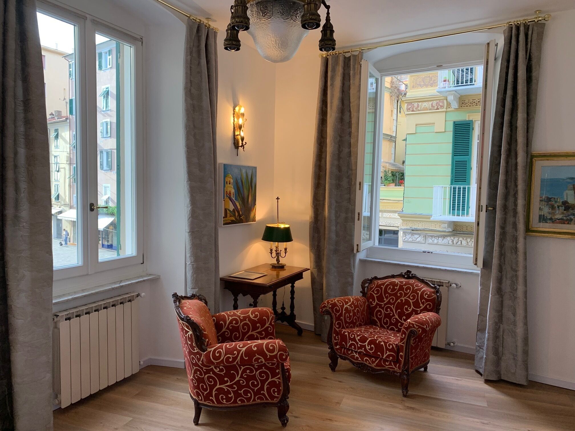 Et værelse med to dekorative stole, et bord med en lampe, et maleri og udsigt til bygninger gennem et vindue.