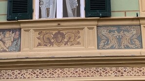 Fachada de edificio con elaboradas contraventanas, molduras decorativas y un motivo floral sobre las ventanas.