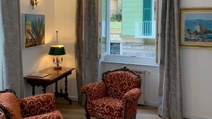 Una habitación con dos sillones decorados, una mesa con lámpara, una lámpara de pared y una ventana con cortinas.
