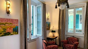 Una habitación con un ventanal grande, dos sillones, una mesa con una lámpara y un cuadro en la pared.