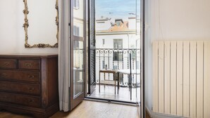 A room with a wooden dresser, a sliding glass door leading to a balcony with a table and chair, and a radiator on the wall. - Easylife - Modern and central apt in Porta Romana (Milano)