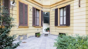 A narrow courtyard with yellow walls and brown shutters, surrounded by greenery. - Easylife - Modern and central apt in Porta Romana (Milano)