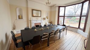 Ein Esszimmer mit einem langen Tisch, Stühlen, einem Kamin und einem großen Fenster.
