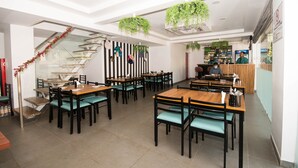 A modern restaurant with multiple dining tables and chairs, a staircase, and hanging plants. - Hotel Vemara (Panaji)