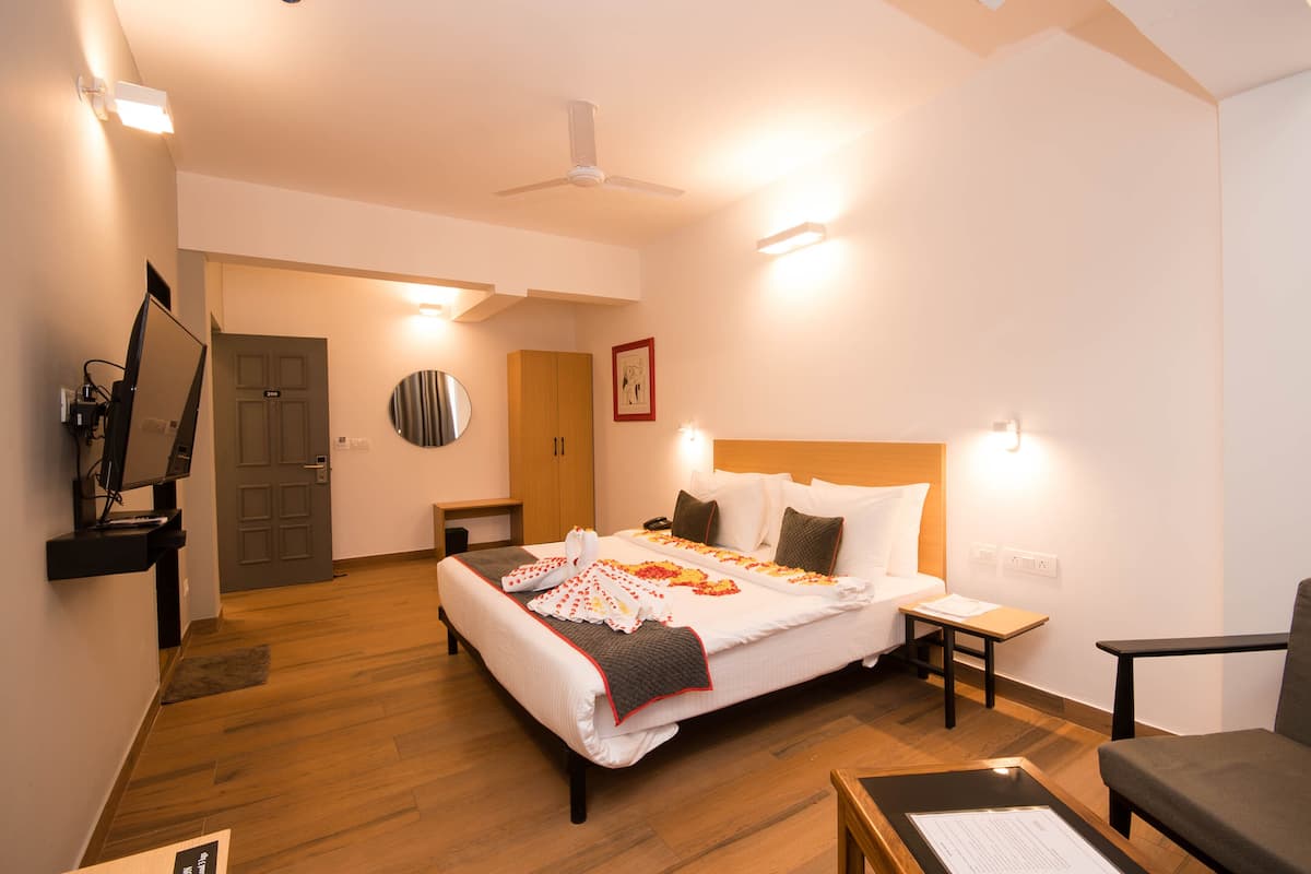 A hotel room with a large bed, a desk, a chair, a television, and a ceiling fan.