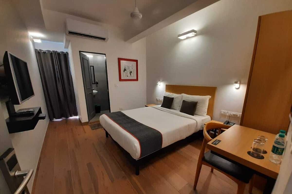 A hotel room with a bed, bedside table, and a desk with a chair.