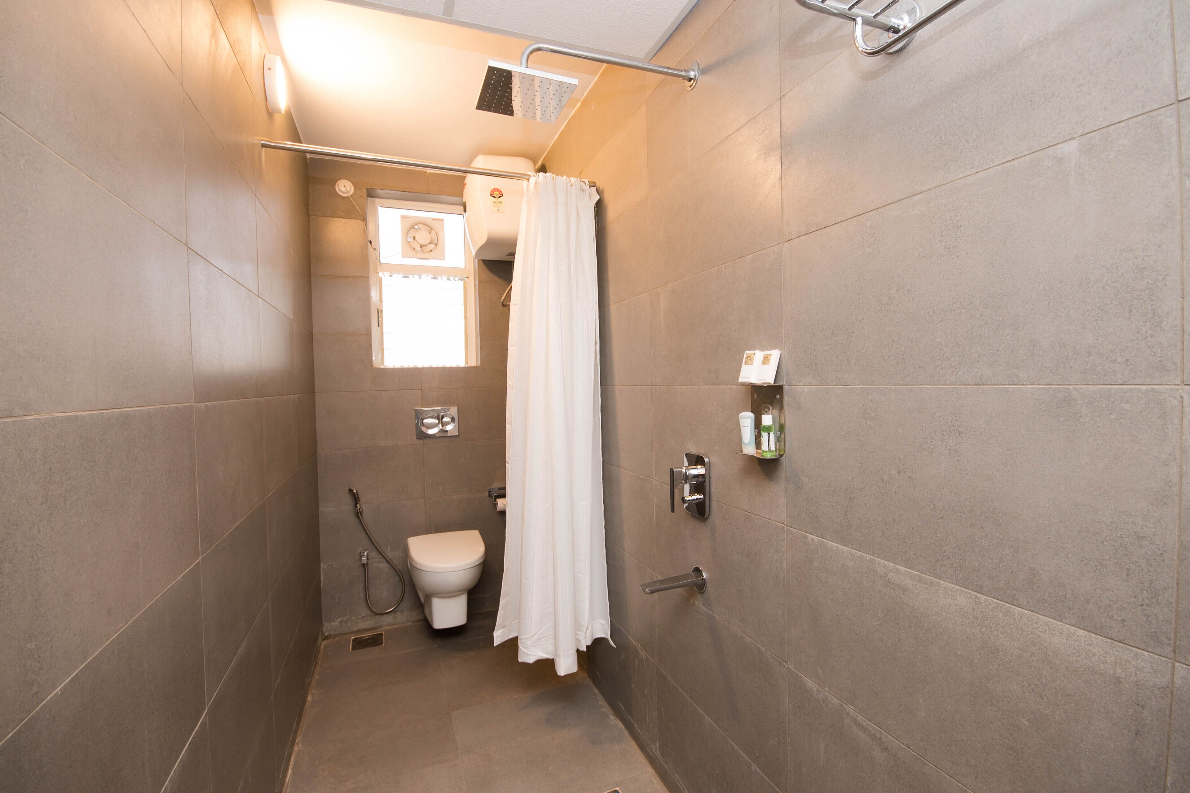 A small, tiled bathroom with a shower, toilet, and a window with a clock.