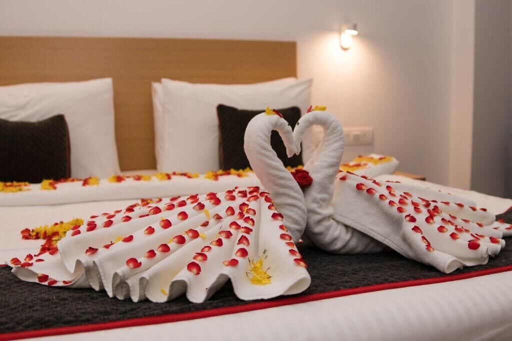 Una cama impecablemente hecha con una toalla dispuesta en forma de corazón y pétalos de rosa.