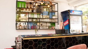 A bar area with shelves of glassware and bottles, a pepsi vending machine, and a hexagonal patterned counter. - Hotel Vemara (Panaji)