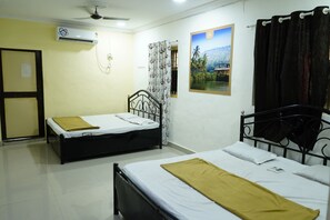 A room with two beds, a ceiling fan, an air conditioning unit, a window with curtains, and a framed picture on the wall. - Vellankani Resort Gorai (Mumbai)