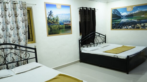 Une chambre avec deux lits, l’un avec un cadre noir et l’autre avec un cadre en métal. Deux affiches sont accrochées aux murs : l’une représente un paysage tropical et l’autre, un paysage montagneux.