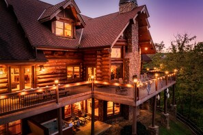 A log cabin with a balcony, outdoor seating, and a stone chimney.