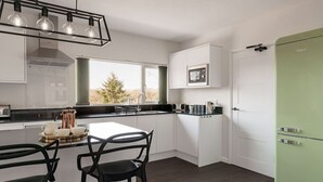 A modern kitchen with white cabinets, a green refrigerator, and a dining area with black chairs and a white table. - Yewbeck: brand new, garden views (Cumbria)