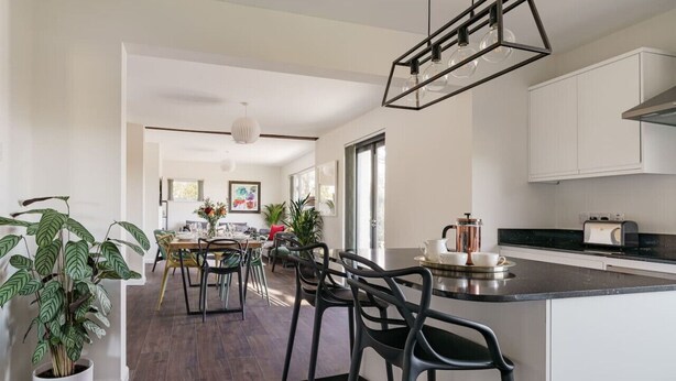 A modern kitchen with a central island, bar stools, and a dining area with a table and chairs. - Yewbeck: brand new, garden views (Cumbria)