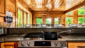 A kitchen with wooden walls, granite countertops, a stove, and a window overlooking greenery.