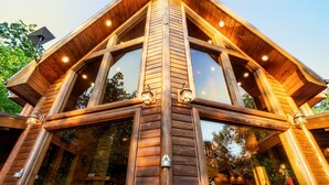 A wooden cabin with large windows and a balcony, featuring a rustic design and outdoor seating.