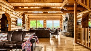 L’intérieur d’une cabane en rondins, avec un plancher en bois, un canapé recouvert d’une couverture, une cheminée et une vue sur l’extérieur.