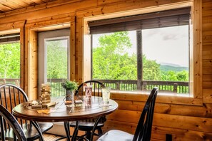 A wooden interior with a round table, chairs, and a view of greenery outside.