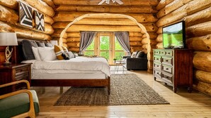 Een slaapkamer in een blokhut met een bed, een kaptafel, een televisie en uitzicht op de natuur.
