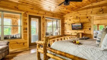 A log cabin bedroom with a wooden bed, a ceiling fan, and large windows.